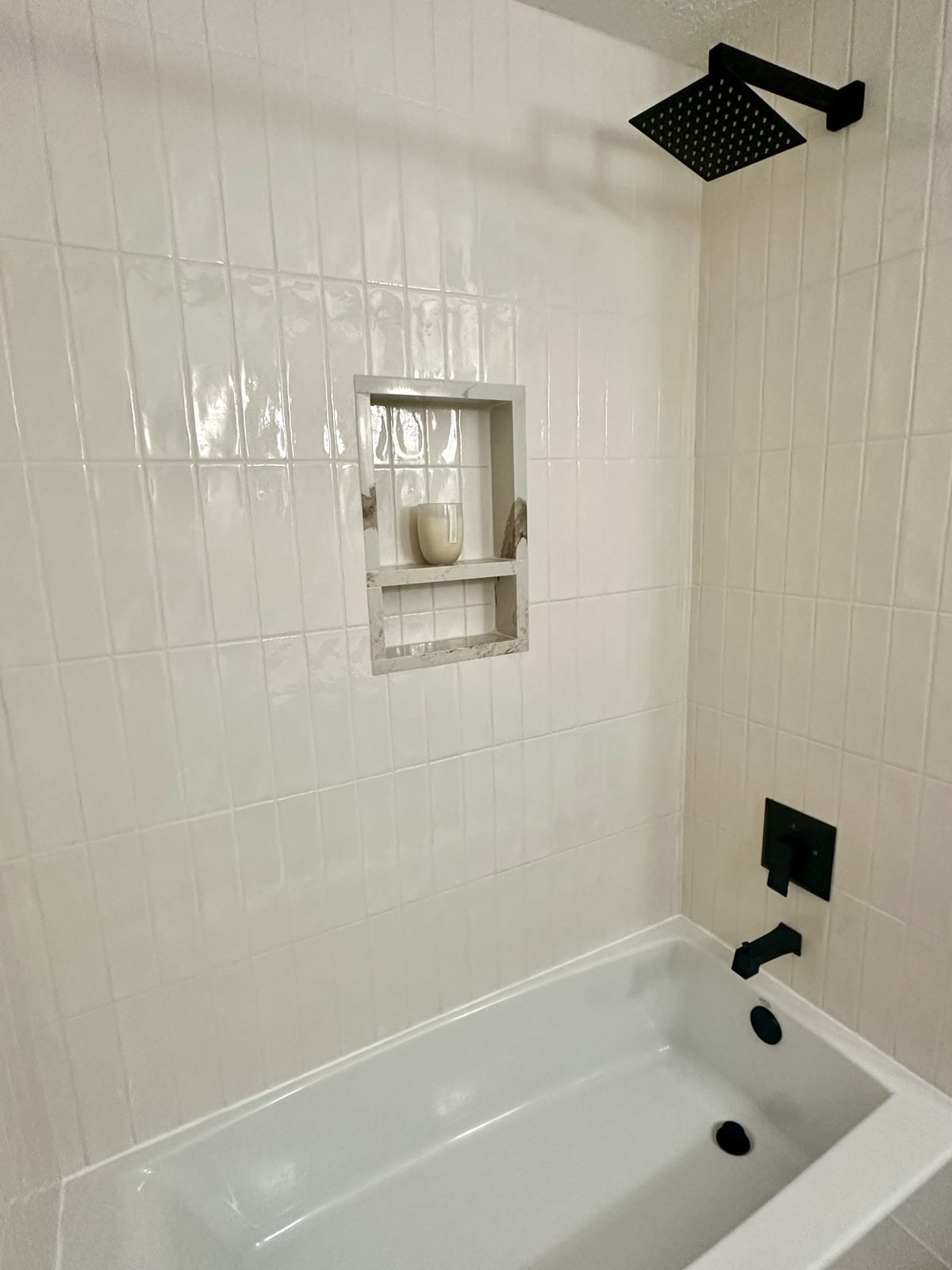 Bathroom tub/shower combo in Winter Haven, FL with vertical stack white tile, matte black fixtures, and marble niche