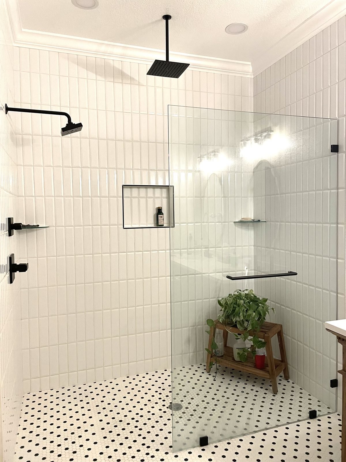 Large walk-in shower in Haines City, FL with double rainfall heads, vertical white tile, and penny tile floor